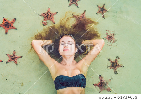Young woman in the sea with red starfishes Young woman in the sea with red starfishes 61734659
