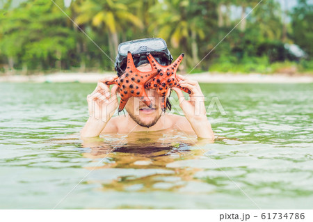Happy young scuba diver holding sea star, smiling, looking at camera 61734786