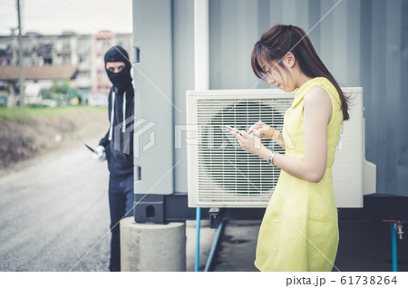 woman walk and chat with friend on smartphone while bandit wear black mask and black clothes holding knife are dodging the corner of the building. 61738264