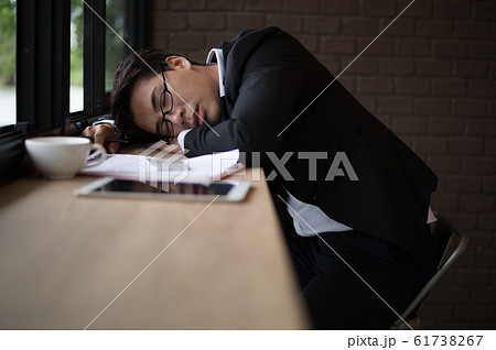 Tired businessman sleeping on the table at workplace with document, laptop and cup of coffee. Tired businessman sleeping on the table at workplace with document, laptop and cup of coffee. 61738267