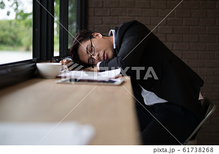 Tired businessman sleeping on counter bar at coffee shop with document, laptop and cup of coffee. 61738268