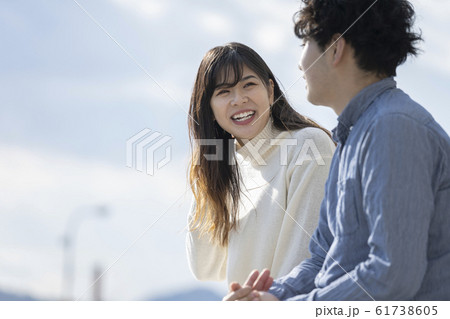 堤防に腰掛け楽しそうに会話をする若いカプル 61738605