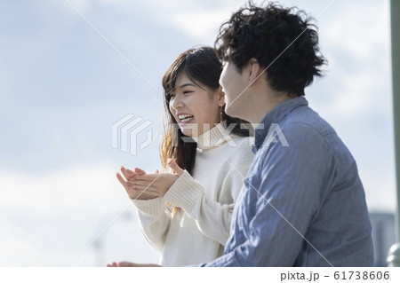 堤防に腰掛け楽しそうに会話をする若いカプル 61738606