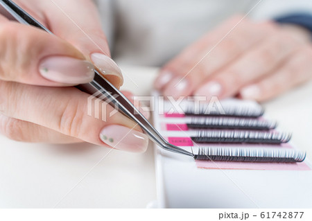 Eyelash Extension Procedure. Close-up of a master at work artificial eyelash extensions material. Hands of the master taking lashes from the set Eyelash Extension Procedure. Close-up of a master at work artificial eyelash extensions material. Hands of the master taking lashes from the set 61742877