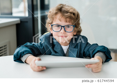 Cute schoolboy with digital tablet looking at you while preparing homework Cute schoolboy with digital tablet looking at you while preparing homework 61744594