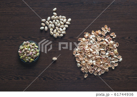 Pistachios are scattered on the brown table. Pistachios are scattered on the brown table. 61744936