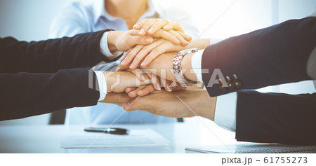 Business team showing unity with their hands together in sunny office. Group of people joining hands and representing concept of friendship, teamwork and partnership Business team showing unity with their hands together in sunny office. Group of people joining hands and representing concept of friendship, teamwork and partnership 61755273