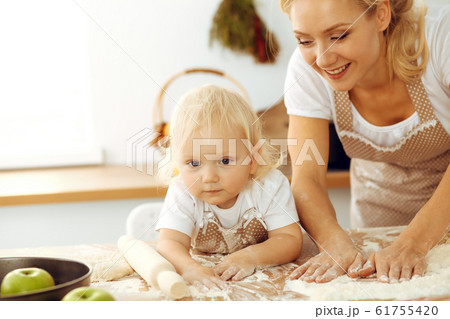 Little girl and her blonde mom in beige aprons playing and laughing while kneading the dough in kitchen. Homemade pastry for bread, pizza or bake cookies. Family fun and cooking concept Little girl and her blonde mom in beige aprons playing and laughing while kneading the dough in kitchen. Homemade pastry for bread, pizza or bake cookies. Family fun and cooking concept 61755420