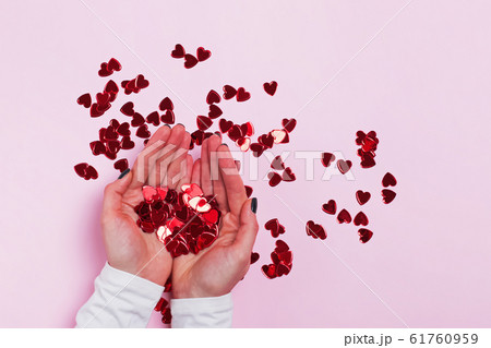 Female hands holdingvibrant red sparkling heart-shaped confetti 61760959