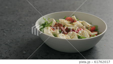ground spices to salad with mozzarella, cherry tomatoes and frisee leaves in white bowl on terrazzo surface ground spices to salad with mozzarella, cherry tomatoes and frisee leaves in white bowl on terrazzo surface 61762017