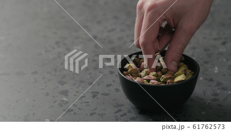 man hand takes pistachio kernels from black bowl on terrazzo surface man hand takes pistachio kernels from black bowl on terrazzo surface 61762573