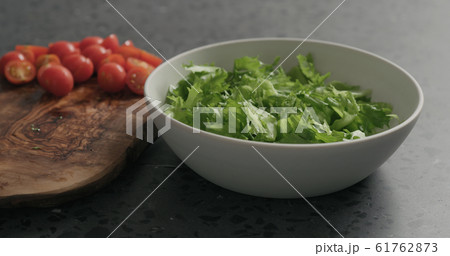 preparing salad with mozzarella, cherry tomatoes and frisee leaves in white bowl on terrazzo surface 61762873