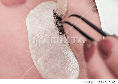Gluing artificial eyelashes with tweezers. Cosmetic procedure. Eyelash extension. 61763532