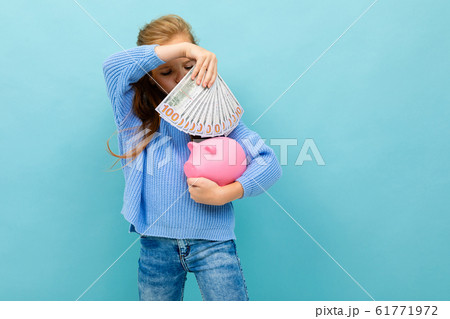 Portrait of little caucasian girl with long hair holds pink pig moneybox isolated on blue background 61771972