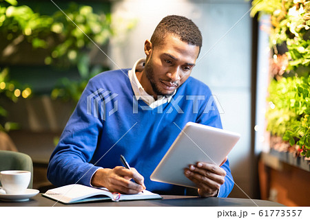 Black man holding tablet and writing in notebook Black man holding tablet and writing in notebook 61773557