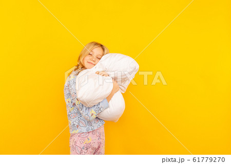 Adorable little girl looking at the camera and hugging a pillow background of a yellow wall 61779270