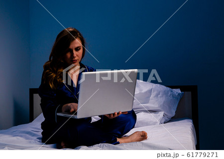 Picture of the woman suffering of insomnia and feeling asleep and working on a laptop at home sitting on the bed. 61779271
