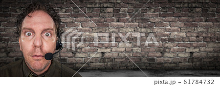 Stunned Businessman Wearing Phone Headset In Front of Brick Wall  61784732