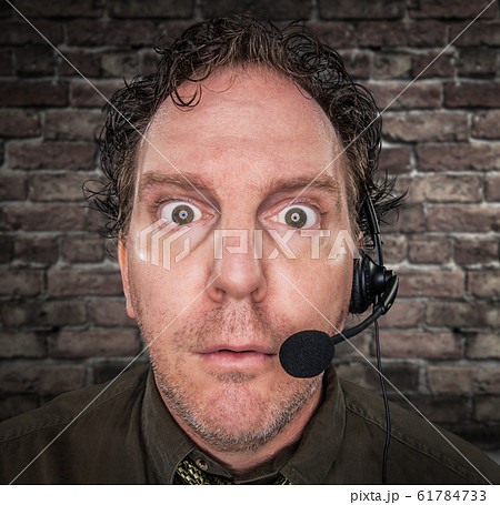 Stunned Businessman Wearing Phone Headset In Front of Brick Wall  61784733