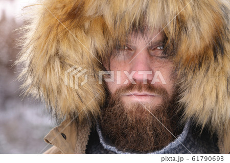 A man dressed in a hooded casual jacket jacket outerwear stern from under the hood a serious portrait of a person in the winter forest. Outdoor time A man dressed in a hooded casual jacket jacket outerwear stern from under the hood a serious portrait of a person in the winter forest. Outdoor time 61790693