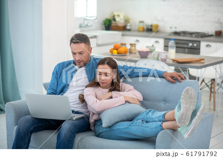 Dad and daughter looking at laptop screen sitting on sofa. 61791792