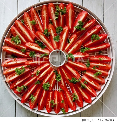 Fresh tomato on food dehydrator tray, ready to dry with salt, parsley, spices on the white wooden background. top view Fresh tomato on food dehydrator tray, ready to dry with salt, parsley, spices on the white wooden background. top view 61798703