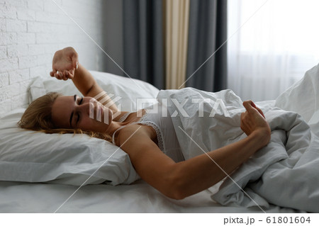 Young woman awakening and stretching in comfortable cozy bed. 61801604