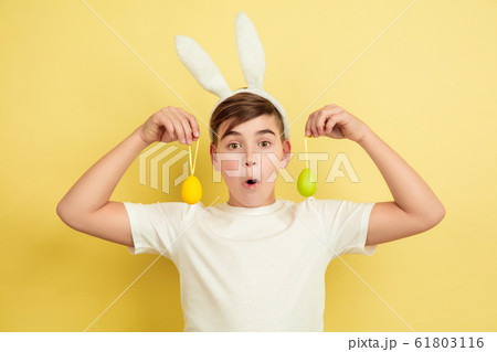Easter bunny boy with bright emotions on yellow studio background 61803116