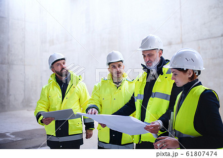 A group of engineers standing on construction site, holding blueprints. 61807474