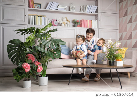 Grandmother sits with granddaughters in the living room. Grandmother sits with granddaughters in the living room. 61807614