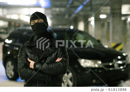 Male criminal in black jacket and balaclava standing on parking area Male criminal in black jacket and balaclava standing on parking area 61813896