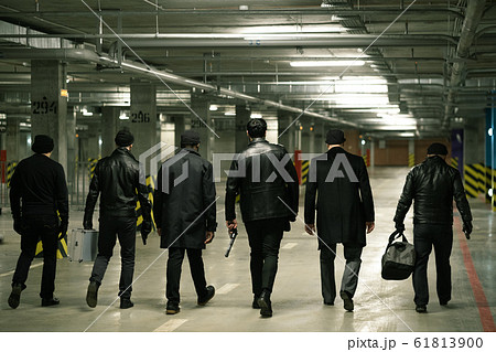 Rear view of gangsters with handguns and bags moving along parking area 61813900