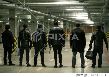Rear view of row of criminals or gangsters in black standing on parking area Rear view of row of criminals or gangsters in black standing on parking area 61813901