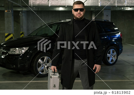 Bearded criminal or agent in black coat and sunglasses moving down parking area Bearded criminal or agent in black coat and sunglasses moving down parking area 61813902