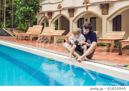 Father and son playing with a remote controlled boat in the pool 61820940