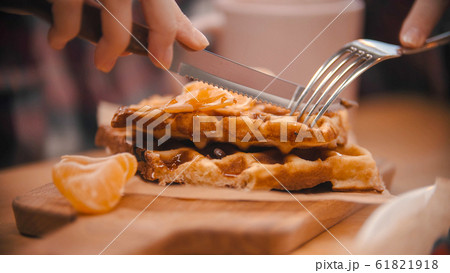 A woman cutting a waffle covered in syrup in the plate 61821918