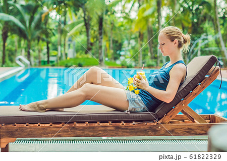 Young woman is holding a smoothie of mango on the background of the pool. Fruit smoothie - healthy eating concept. Close up of detox smoothie with mango Young woman is holding a smoothie of mango on the background of the pool. Fruit smoothie - healthy eating concept. Close up of detox smoothie with mango 61822329