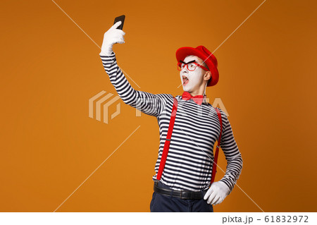 Young mime in white gloves and red hat takes selfie on orange background 61832972