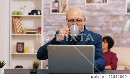 Old man enjoying a cup of coffee while working on laptop 61833069