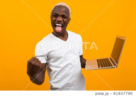 joyful black American with a beautiful snow-white smile in a white T-shirt with a laptop on an 61837790