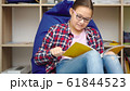 Girl is reading book while sitting in room 61844523