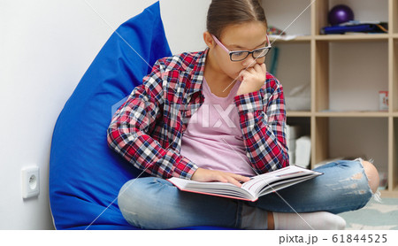 Girl is reading book while sitting in room 61844525