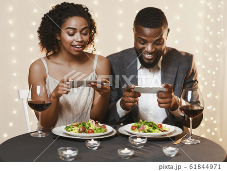 Young couple sitting in restaurant and taking pictures of food 61844971