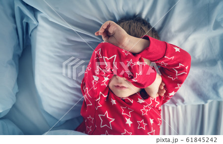 Sleepy boy lying in bed with blue beddings 61845242