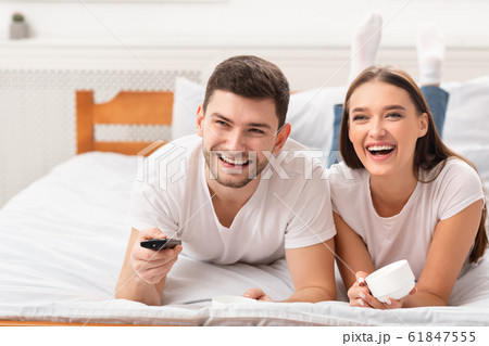 Happy Couple Watching TV Lying In Bed Indoor 61847555