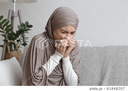 Sick muslim woman blowing runny nose to napkin at home 61848207