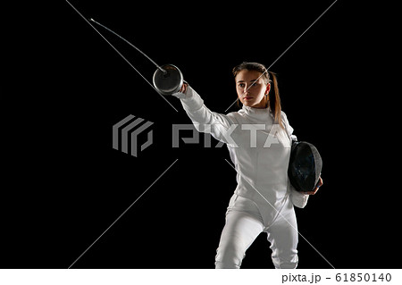 Teen girl in fencing costume with sword in hand isolated on black background Teen girl in fencing costume with sword in hand isolated on black background 61850140