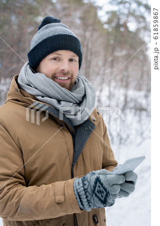 Young man in grey beanie, scarf, gloves warm jacket scrolling in smartphone 61859867