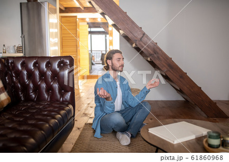 Relaxed young man meditating in his appartment Relaxed young man meditating in his appartment 61860968