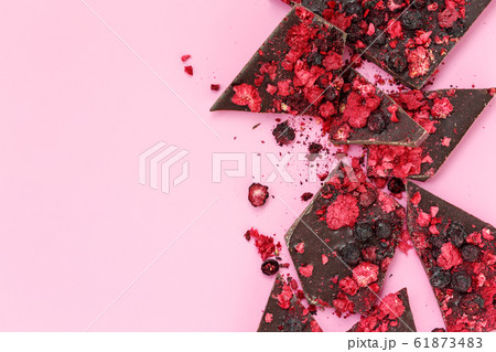 Broken black chocolate bar pieces with scattered dried red berries on pink background, flat lay Broken black chocolate bar pieces with scattered dried red berries on pink background, flat lay 61873483